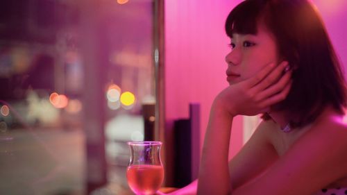 Smiling woman with drink sitting at illuminated nightclub