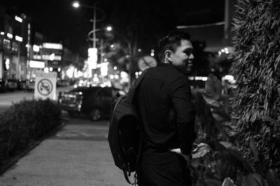 Smiling man looking away by tree in city at night