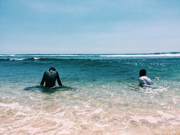Boys swimming in sea against sky