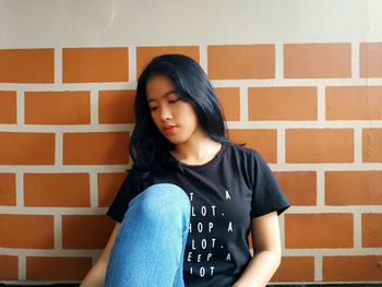 Young woman contemplating while sitting against brick wall