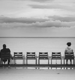 Rear view of people sitting on bench by sea