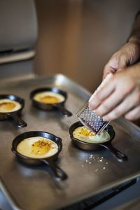 Man grating cheese on half fried eggs on baking sheet