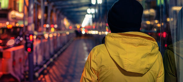 Rear view of woman in warm clothes standing in city at night