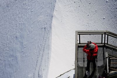 High angle view of man photographing snow while standing on steps 