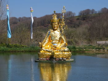Statue by lake against sky