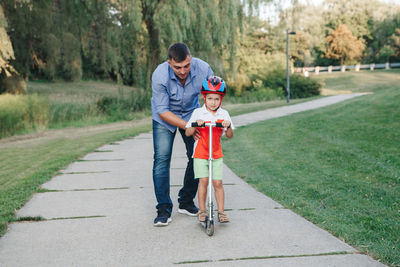 Caucasian father dad training teaching boy son to ride scooter. preschooler child kid in helmet 