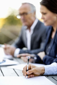 Cropped image of businessman writing on document with colleagues at table