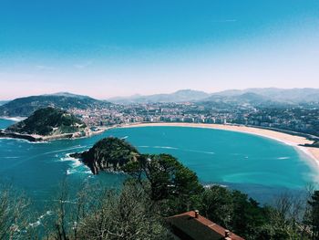 Sea by city and mountains against clear blue sky