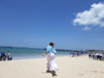 Rear view of woman walking on beach against sky