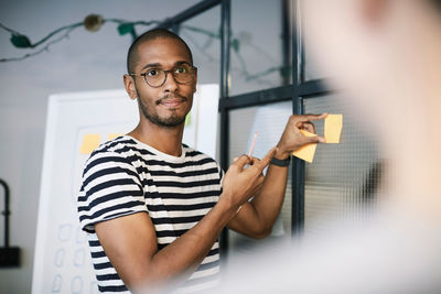 Creative businessman showing adhesive note to colleague in office