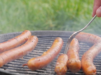 Cropped image of person cooking sausages on barbecue grill