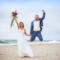 Portrait of cheerful bride and bridegroom at beach against sky