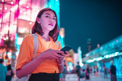 Portrait of woman using mobile phone in city at night