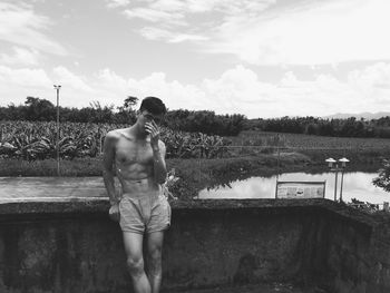 Full length of shirtless man standing by lake against sky