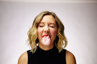 Close-up of woman blowing bubble gum against white background