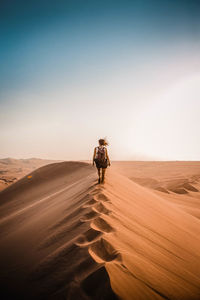 Rear view of woman walking on sand dune in desert