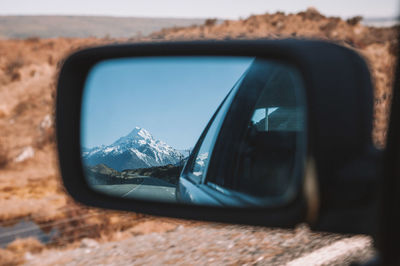 Reflection of snowcapped mountain on side-view car mirror 