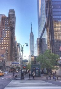 People walking on road by buildings against sky in city