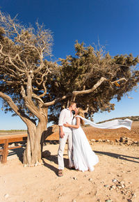 Woman standing by tree against clear blue sky