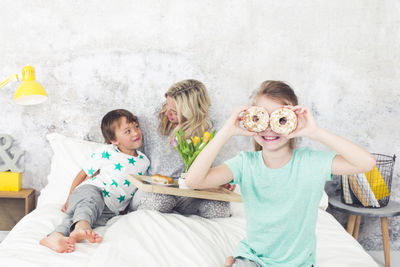 Portrait of smiling girl with donut sitting with family on bed