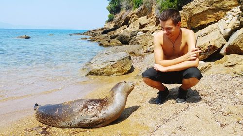 Young man with seal at beach against sky