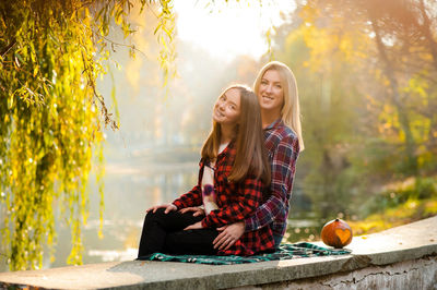 Young woman smiling while sitting on tree during autumn