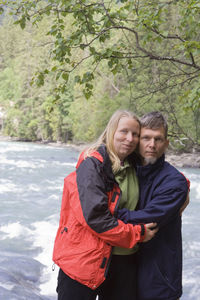 Portrait of couple in warm clothing standing by river in forest