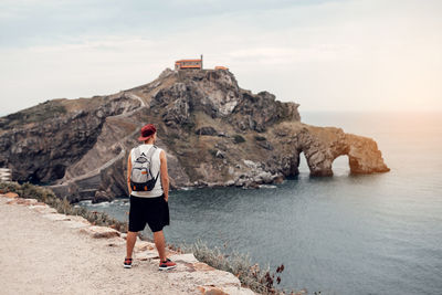 Rear view of man standing on rock by sea against sky