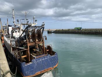 Fishing boat moored on pier by sea against sky