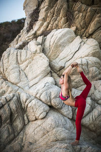 Woman practicing king dancer pose on rocks