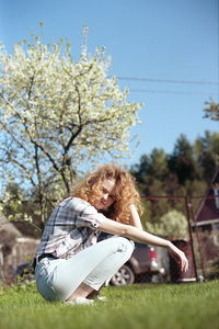 Woman sitting on field by tree against sky