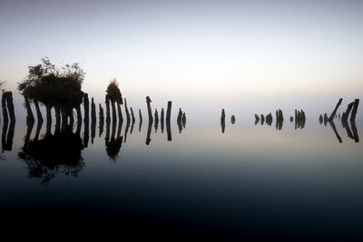 Silhouette wooden posts in lake against sky at sunset