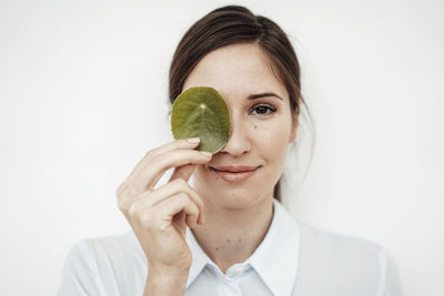 Businesswoman holding leaf on her eye against white background in studio