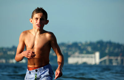 Portrait of shirtless boy walking in sea against sky