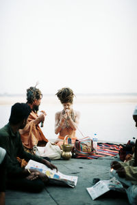 People sitting by sea against clear sky