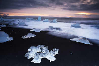 Ice at beach against sky during sunset