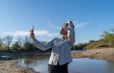 Man photographing with mobile phone against sky