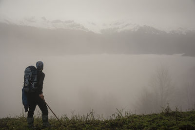 Side view of man with backpack walking on field by lake during foggy weather