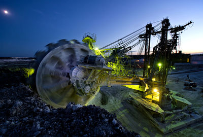 Illuminated machine at mining field against sky at dusk