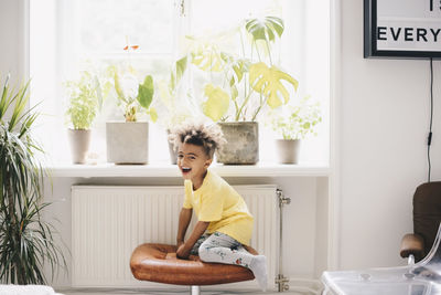 Happy boy sitting on chair by window at home