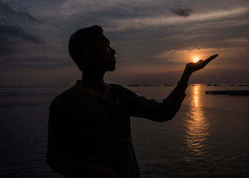 Silhouette man standing on beach against sky during sunset