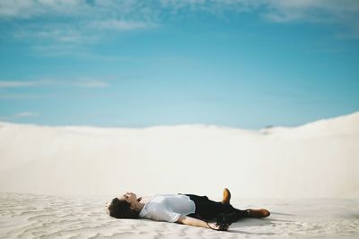 Full length of woman holding camera lying on sand at desert against sky