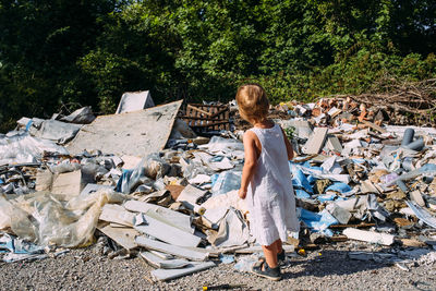 Little girl at a dump among a heap of scattered garbage in the forest.