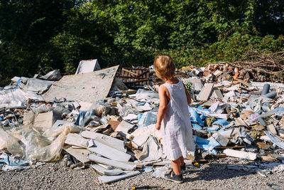 Little girl at a dump among a heap of scattered garbage in the forest.