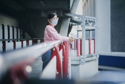 Woman wearing mask standing by railing