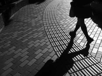 Low section of silhouette woman walking on sidewalk