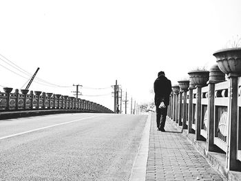Rear view of man walking on bridge in city against clear sky