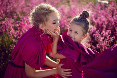 Happy family mother and daughter in pink dresses are sit in a field with flowers and big balloons 