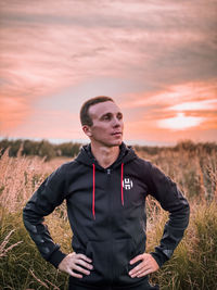 Young man standing on field against sky during sunset