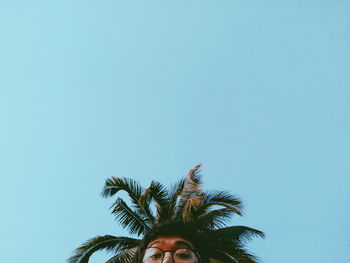 Cropped image of man and palm tree against clear blue sky